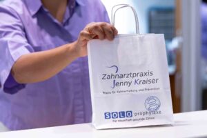 Eine Person mit hellem Hemd hält eine weiße Tüte mit blauer Schrift in der Hand